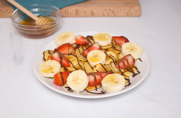Μοντέρνο φαγητό - δημητριακά για τηγανίτες. Σωρός από μίνι τηγανίτες δημητριακών σε ένα λευκό πιάτο, αντίγραφο χώρο. Φράουλες, μπανάνες και μέλι. Ένα όμορφο και υγιεινό πρωινό. - Φωτογραφία, εικόνα