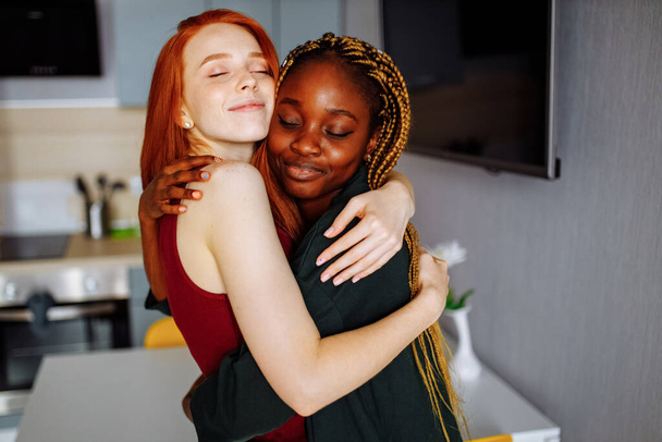 Multiracial couple girlfriends in love embracing in room - Фото, изображение
