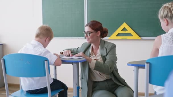 μαθητές στην τάξη στο μάθημα μαθηματικών, δάσκαλος σε γυαλιά δείχνει κάρτες με αριθμούς και βοηθά να κάνει μετράνε αγόρι με σύνδρομο down στο σχολείο - Πλάνα, βίντεο