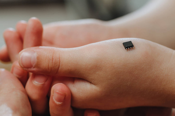 Ein kleiner schwarzer Chip liegt auf der Handfläche eines Kindes. Chipisierung von Menschen nach einer Coronavirus-Epidemie.  - Foto, Bild