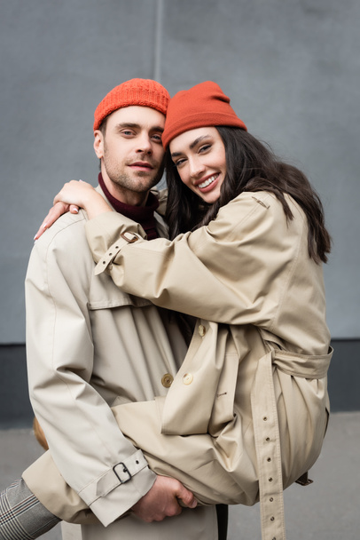 stylish man holding in arms woman in beanie hat and trench coat  - Fotó, kép
