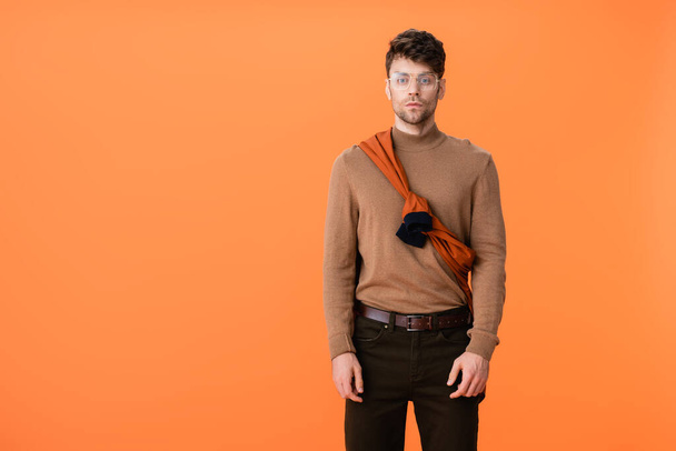 trendy man in autumn outfit and glasses isolated on orange  - Foto, Imagen