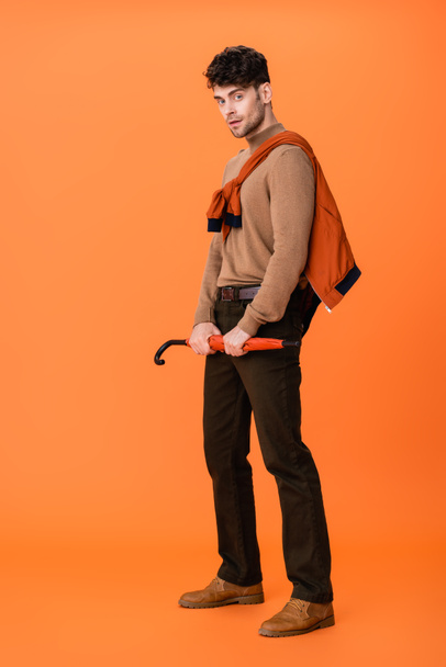 full length of trendy man in autumn outfit holding umbrella on orange  - Photo, Image