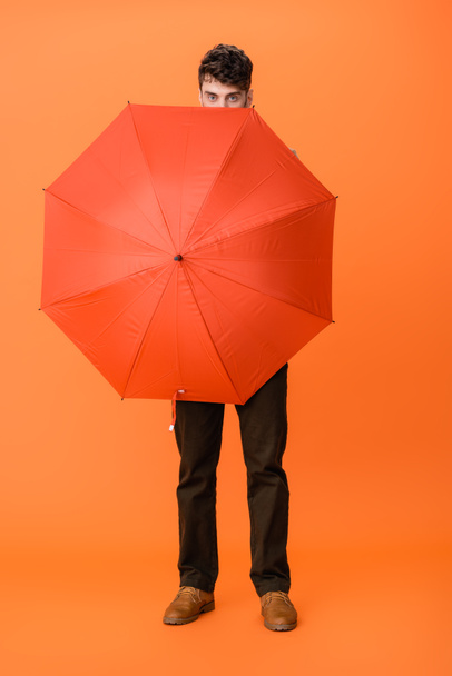 full length of man in brown pants holding umbrella on orange  - Fotografie, Obrázek