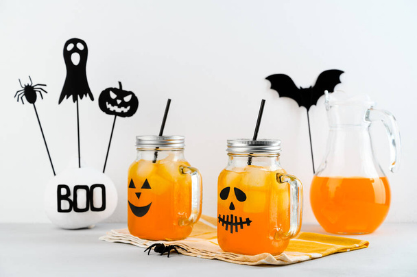 Halloween-Kürbis vereiste Mocktails in Glasgefäßen mit gruseligen Gesichtern auf einem weißen Tisch. - Foto, Bild