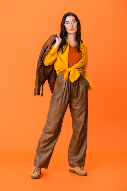 full length of young woman in autumn outfit holding leather jacket on orange  - 写真・画像