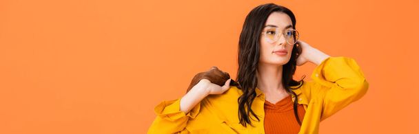 panoramic crop of trendy woman in glasses and autumn outfit holding leather jacket isolated on orange  - Foto, Imagen