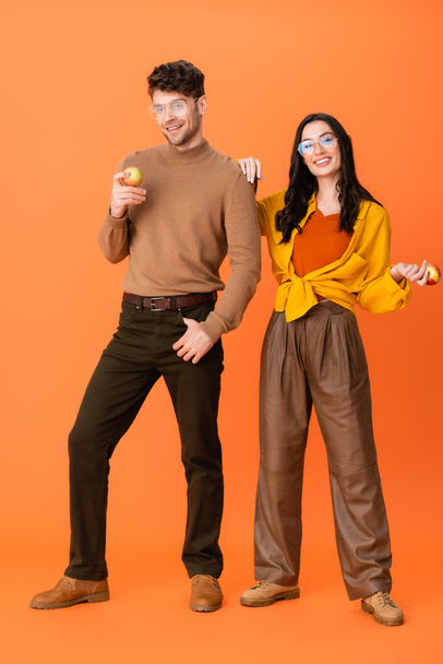 pełna długość modnej pary w okularach i jesiennym stroju gospodarstwa jabłka na pomarańczy - Zdjęcie, obraz