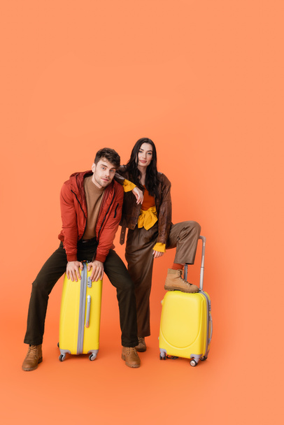 piena lunghezza di coppia alla moda in abito autunno seduto bagaglio giallo su arancione  - Foto, immagini