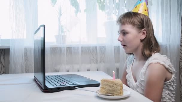 chica se sienta a la mesa con el ordenador portátil, sopla vela encendida en pastel de cumpleaños - Metraje, vídeo