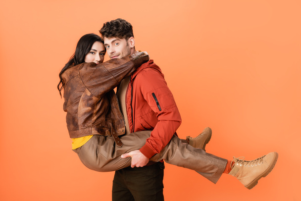 módní muž drží v náručí žena v podzimním oblečení na oranžové  - Fotografie, Obrázek