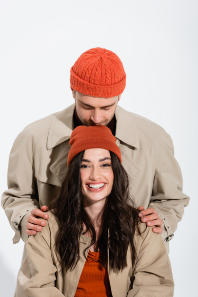 мужчина в шляпе-шапочке целует голову радостной женщины, изолированной на белом - Фото, изображение