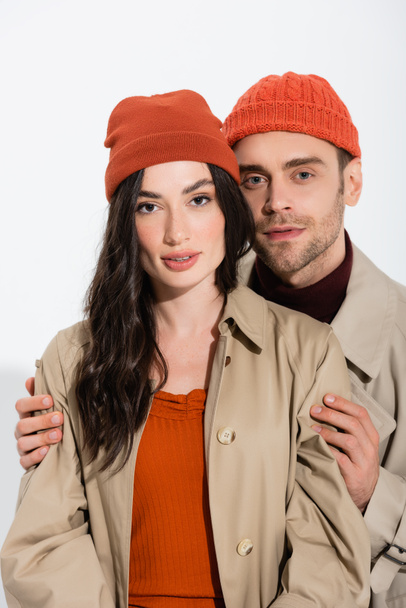 trendy man in beanie hat touching stylish young woman on white - Valokuva, kuva