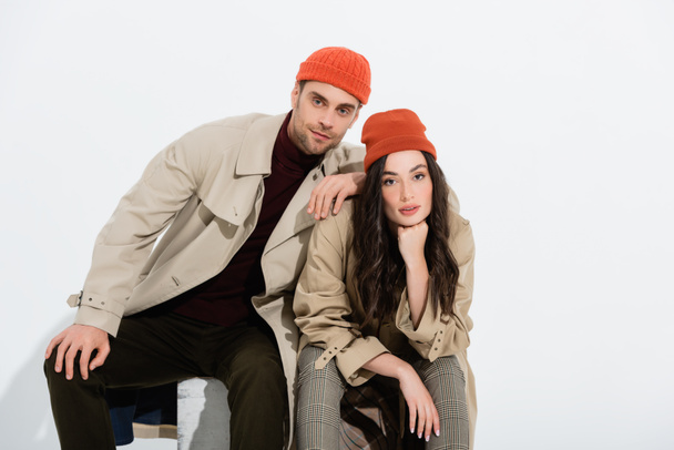 trendy man in beanie hat leaning on brunette woman on white  - Photo, Image