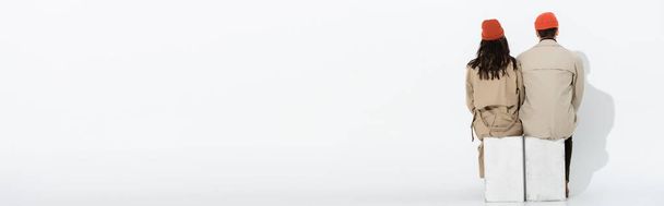 ιστοσελίδα κεφαλίδα του trendy ζευγάρι σε beanie καπέλα και καμπαρντίνες κάθεται σε λευκό  - Φωτογραφία, εικόνα