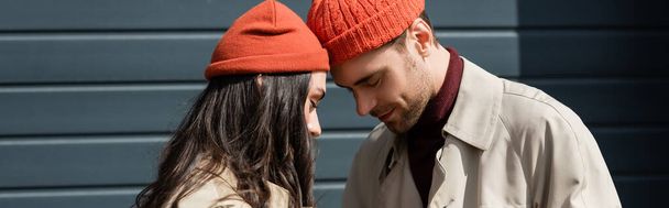 panoramic crop of stylish couple in hats leaning on each other outside - Φωτογραφία, εικόνα