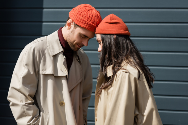 stylish couple in trench coats and hats leaning on each other outside - Fotó, kép