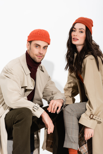 couple in beanie hats and trench coats looking at camera on white  - Fotó, kép