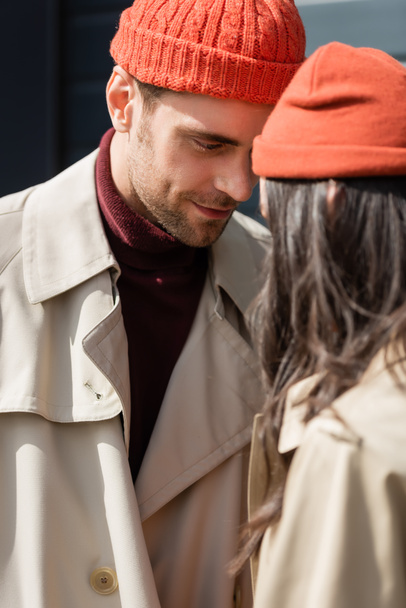 enfoque selectivo de hombre con estilo en gabardina y sombrero mirando a la mujer fuera - Foto, Imagen
