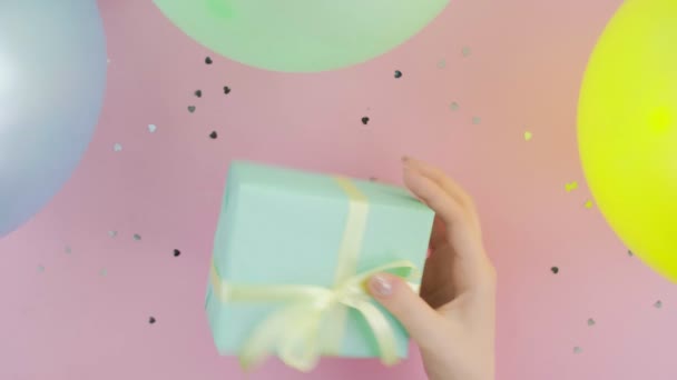 Female hand shakes Christmas birthday gift box wrapped in green paper on pink background top view - Footage, Video