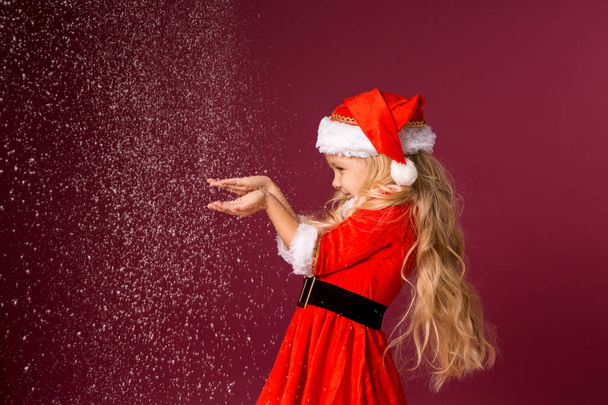 Cute little blond girl in a Santa's costume on red background with 2020 big numbers. Celebration of Christmas and new year concept - Photo, image