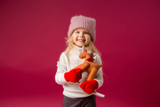 Kleines fröhliches Mädchen in warmer Winterkleidung, das seinen Spaß auf rotem Hintergrund hat. Leerzeichen-Bild mit Platzierung für Ihren Text oder Ihre Anzeige kopieren - Foto, Bild