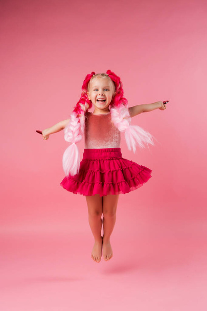 Little happy girl with big pink braids having fun with heart shaped lollipops. Picture with space for text isolated on pink background, children's emotions concept. - Φωτογραφία, εικόνα