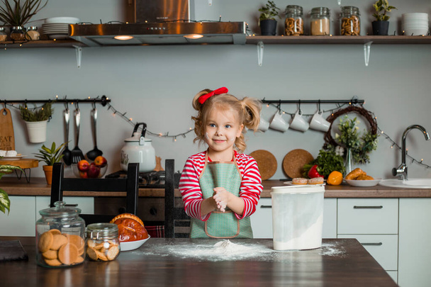 Little blond girl with ingredients for cooking at modern stylish kitchen. Cute mother's helper - Фото, изображение