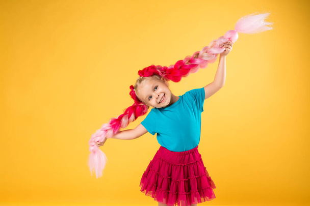 Šťastná dívka s velkými růžovými copánky baví na oranžovém pozadí, Dětské emoce koncept. - Fotografie, Obrázek