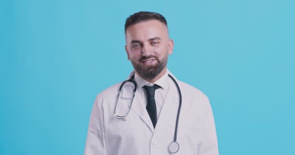 Přátelský lékař středního věku přikyvující hlavou ano a usmívající se na kameru, modré pozadí studia - Záběry, video