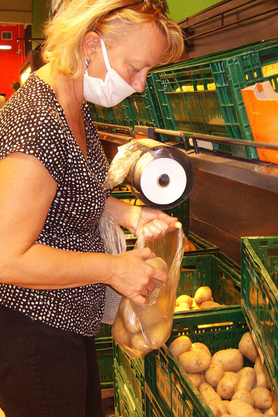 une femme masquée met des pommes de terre dans un sac dans un supermarché - Photo, image