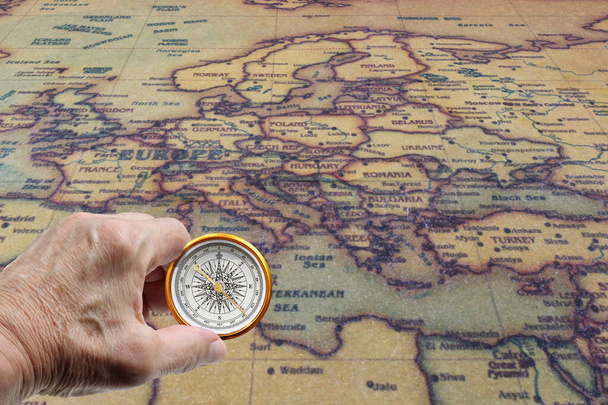 Klasyczny okrągły kompas w dłoni na tle starej zabytkowej mapy świata jako symbol turystyki z kompasem, podróży z kompasem i zajęć na świeżym powietrzu z kompasem - Zdjęcie, obraz