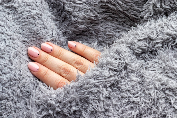 Vrouwelijke hand in een grijze pluizige gebreide trui stof met trendy mooie manicure - roze naakte nagels met zwarte kleine stippen met kopieerruimte. Selectieve focus. Close-upzicht - Foto, afbeelding