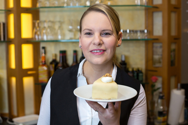 Официантка в кафе представляет торт на тарелке
 - Фото, изображение