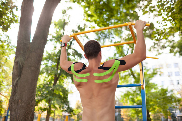 Unrecognizable man pulling up with kinesiological taping outdoors. - 写真・画像