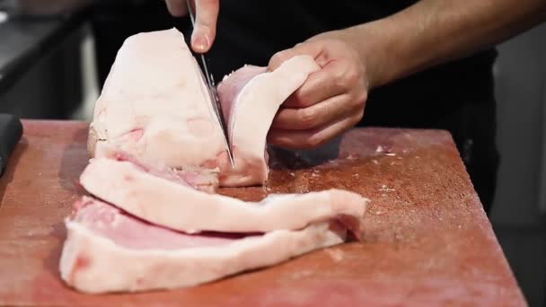 Rauwe varkenssteak op een houten plank. Slachter snijdt rauw vlees met een mes in slow motion - Video