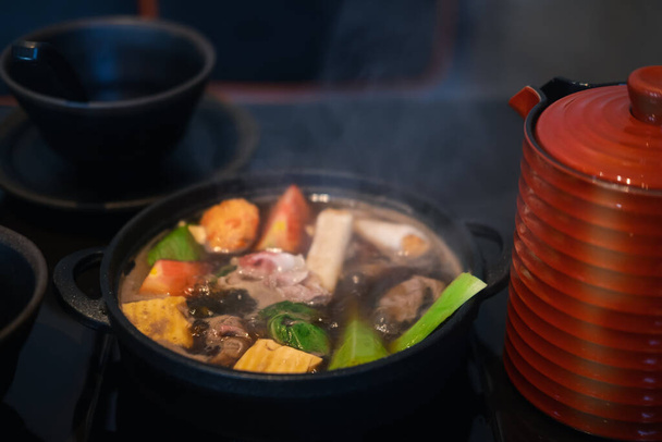日本のすき焼き豚肉、牛肉、野菜を混ぜ合わせ、黒スープを伝統的な鋳鉄製の鍋で煮込みます。選択的焦点 - 写真・画像
