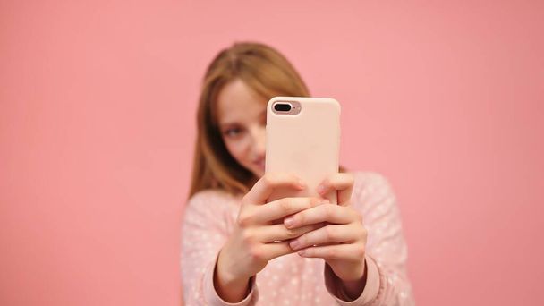 Молода біла жінка використовує смартфон і фотографує. Ізольовані на рожевому фоні
 - Фото, зображення