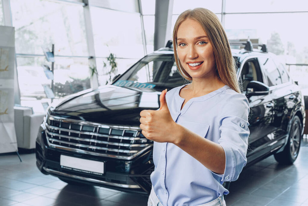 Attractive young female car dealer standing in showroom - Фото, изображение