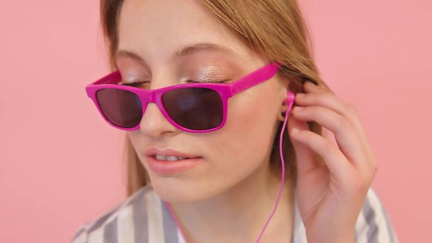 Όμορφη νεαρή καυκάσια γυναίκα ακούει τη μουσική με τα ακουστικά. απομονωμένο σε ροζ φόντο - Φωτογραφία, εικόνα