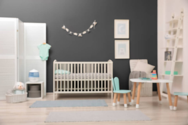 Blurred view of cute baby room interior with modern crib near dark wall - Photo, image