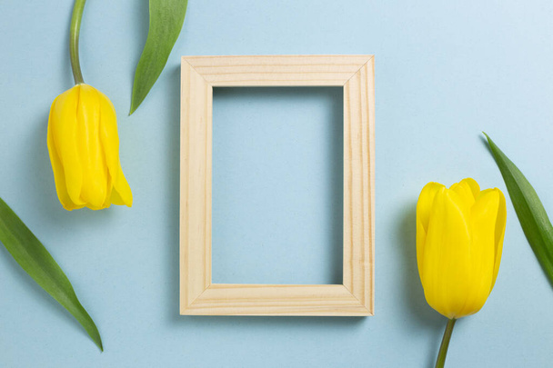 Marco de fotos de madera con flores de tulipán amarillo sobre fondo azul. vista superior, espacio de copia - Foto, imagen