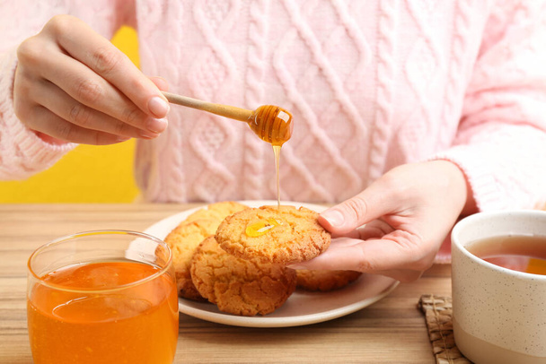 Woman pouring honey onto cookie at wooden table, closeup - Foto, immagini
