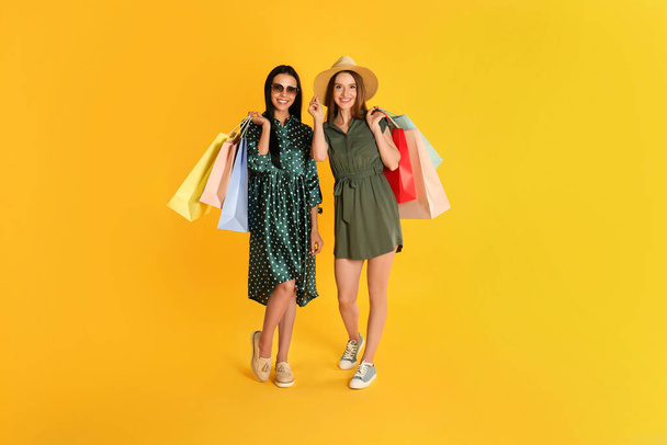 Beautiful young women with paper shopping bags on yellow background - Foto, Imagem