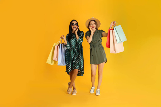 Beautiful young women with paper shopping bags on yellow background - Φωτογραφία, εικόνα