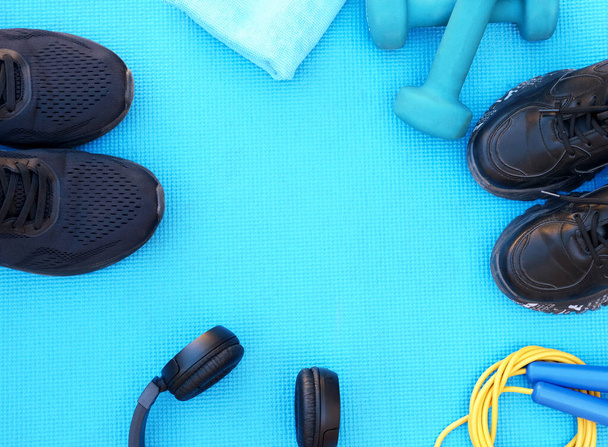 concepto de fitness sport, espacio para texto, zapatillas negras, pesas azules, auriculares, cuerda de salto de fitness sobre plantilla de fondo azul - Foto, Imagen