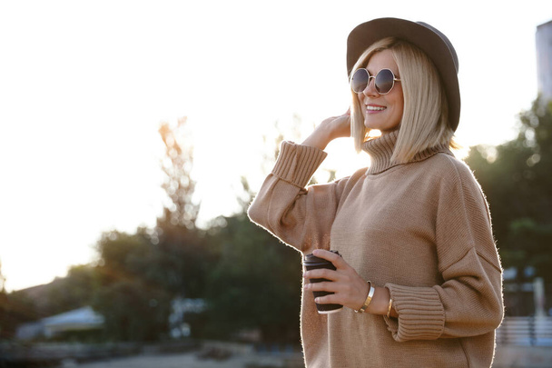 Woman in stylish sweater with cup of coffee on city street - Foto, Bild