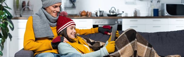 horizontal concept of excited couple in warm hats and gloves watching movie on laptop in cold kitchen - Foto, Imagem