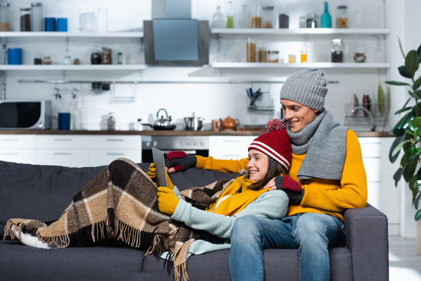 couple excité dans des chapeaux chauds et gants regarder film sur ordinateur portable dans la cuisine froide - Photo, image