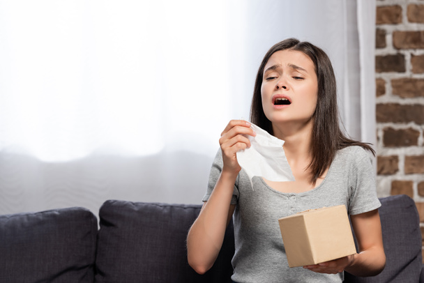 sick young woman sneezing while holding paper napkin at home - Foto, Bild